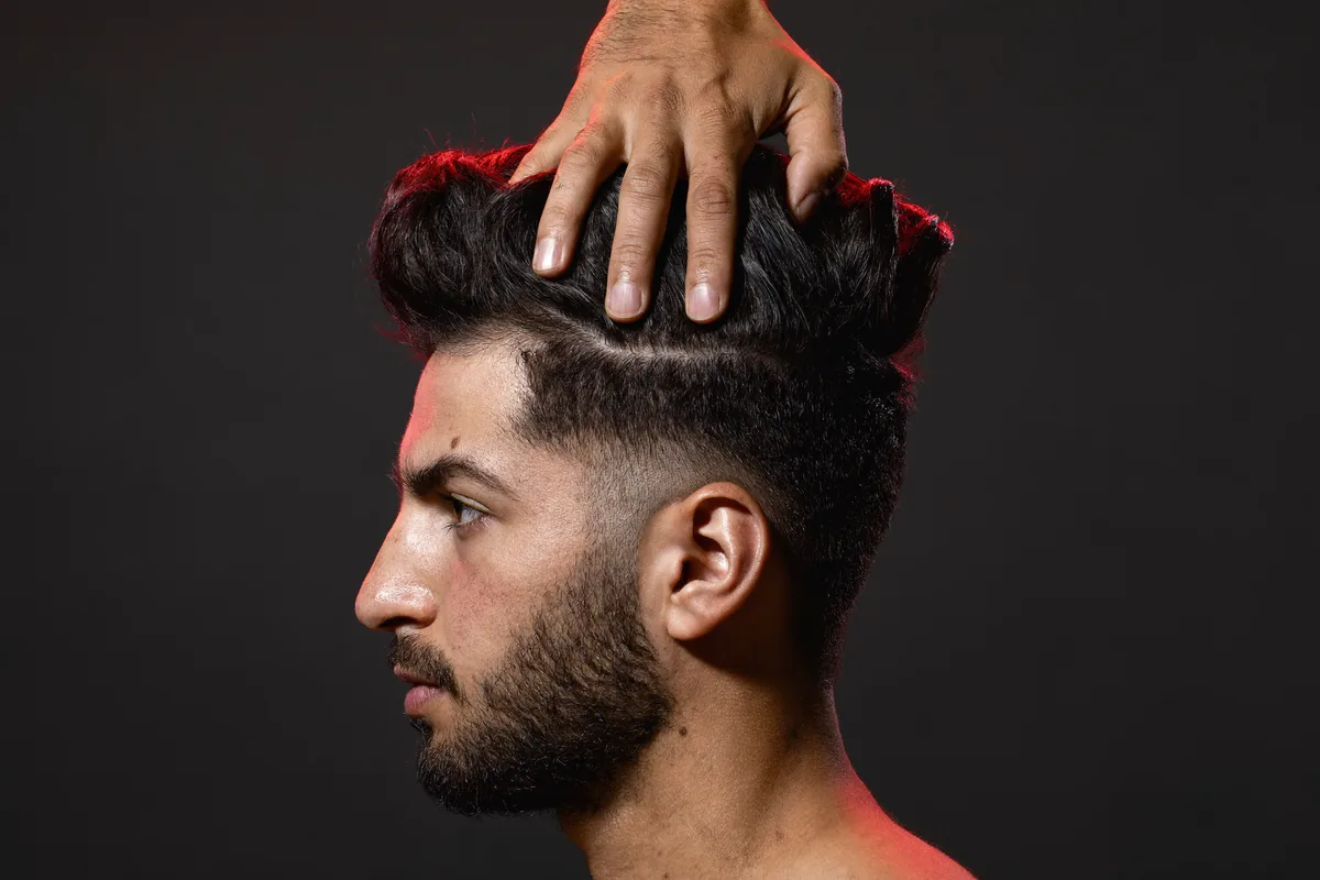 A flat hand pressing down on a tall styled quiff, the hair holding its shape under the pressure